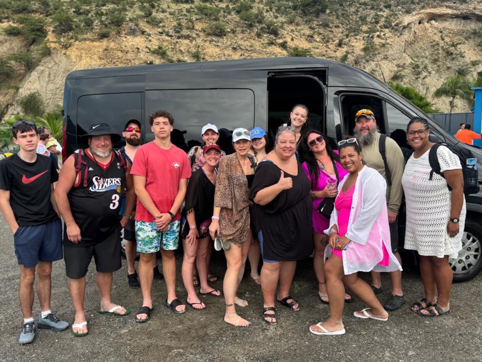 Large smiling tour group beside a black passenger van in Sint Maarten